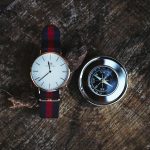A wristwatch and a compass placed on a wooden stump, captured from above.